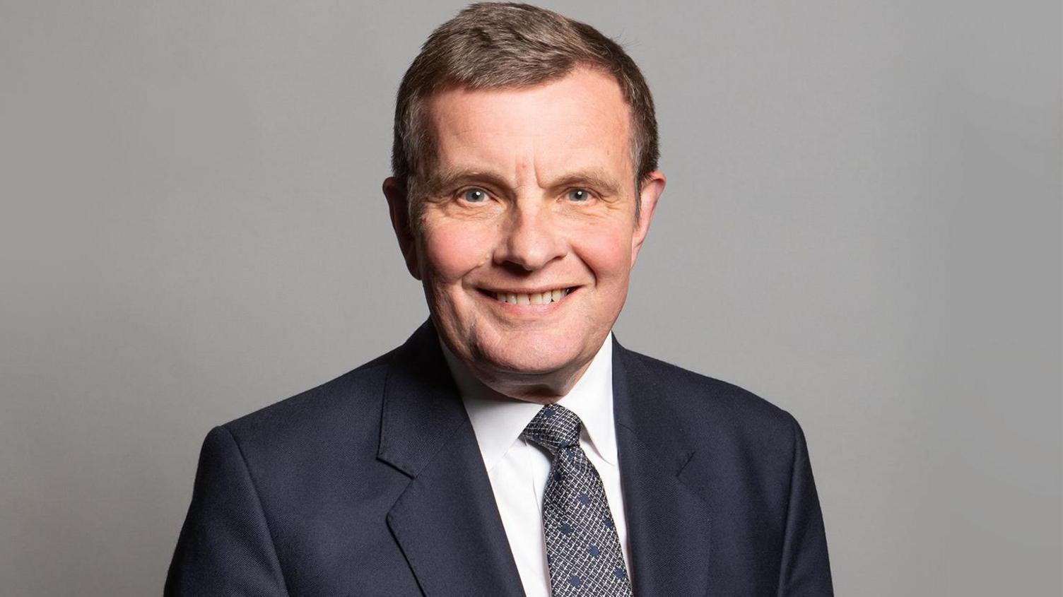 Profile photo of David Jones looking into camera wearing a dark suit, white shirt and grey tie, taken during his time in parliament.