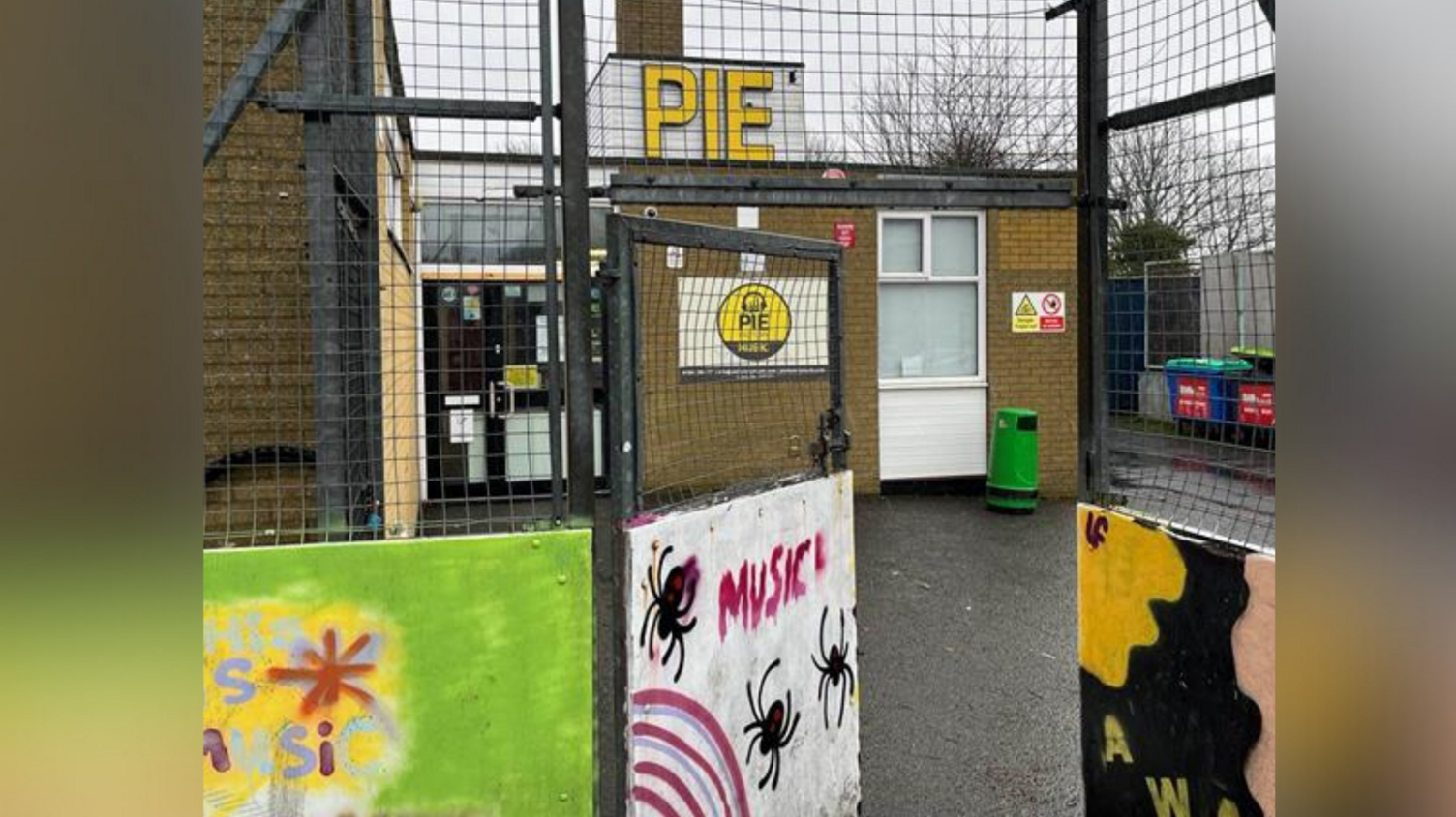 An external image of the Pie Factory at Ramsgate Youth Centre. The building has two signs stating 'Pie' - one larger on the roof and one to the right of the front door. The gate entrance features a number of paintings.