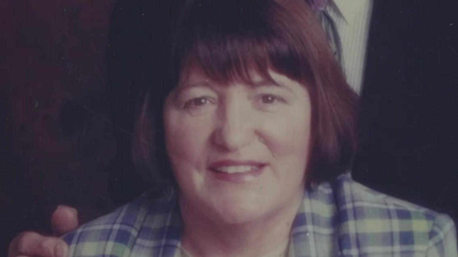 Marlene with brown bobbed hair and brown eyes smiling wearing a blue and white checked shirt