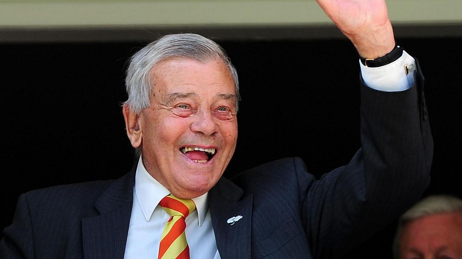 A smiling Dickie Bird, in a smart jacket and yellow and orange MCC tie, gives a wave