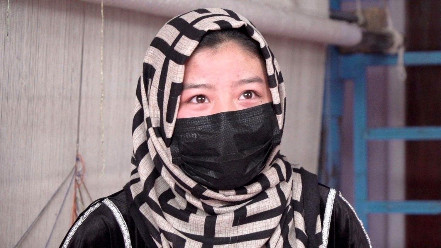 A woman wears a headscarf and face mask