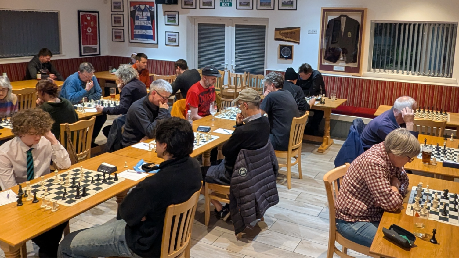 Llun yn dangos ystafell llawn pobl yn chwarae gwyddbwyll, mewn clwb rygbi.