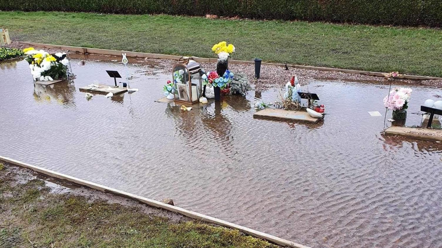 Graves with floral tributes surrounded by water.