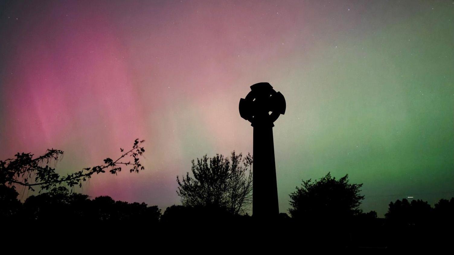 A war memorial and trees in silhouette against a purple and green sky.