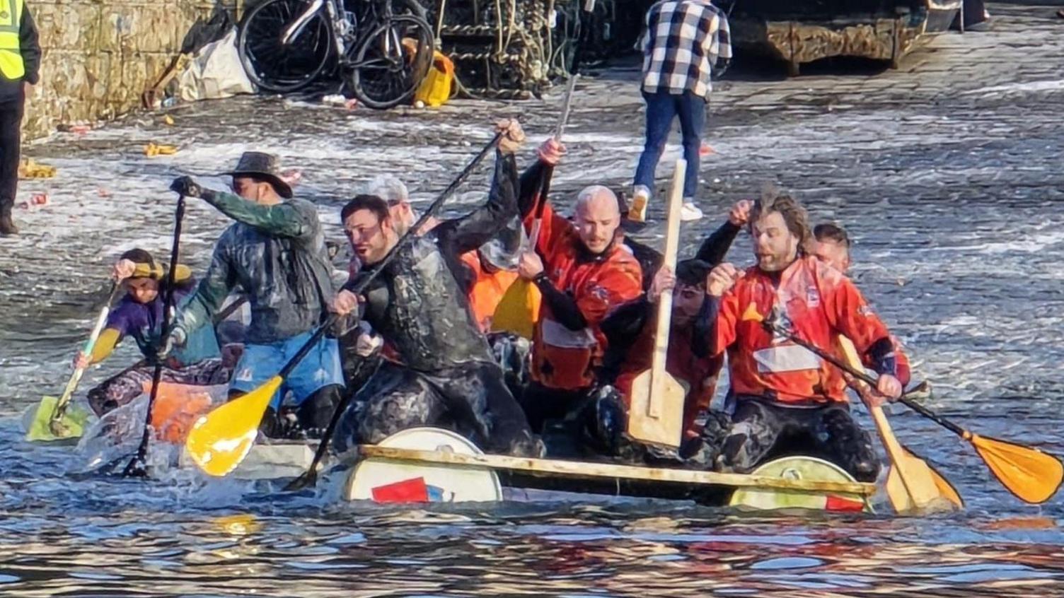 Several people on board a racing raft with awes in their hands. 