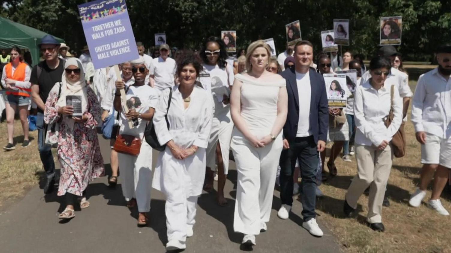 A crowd of people walk along the street in white, holding placards