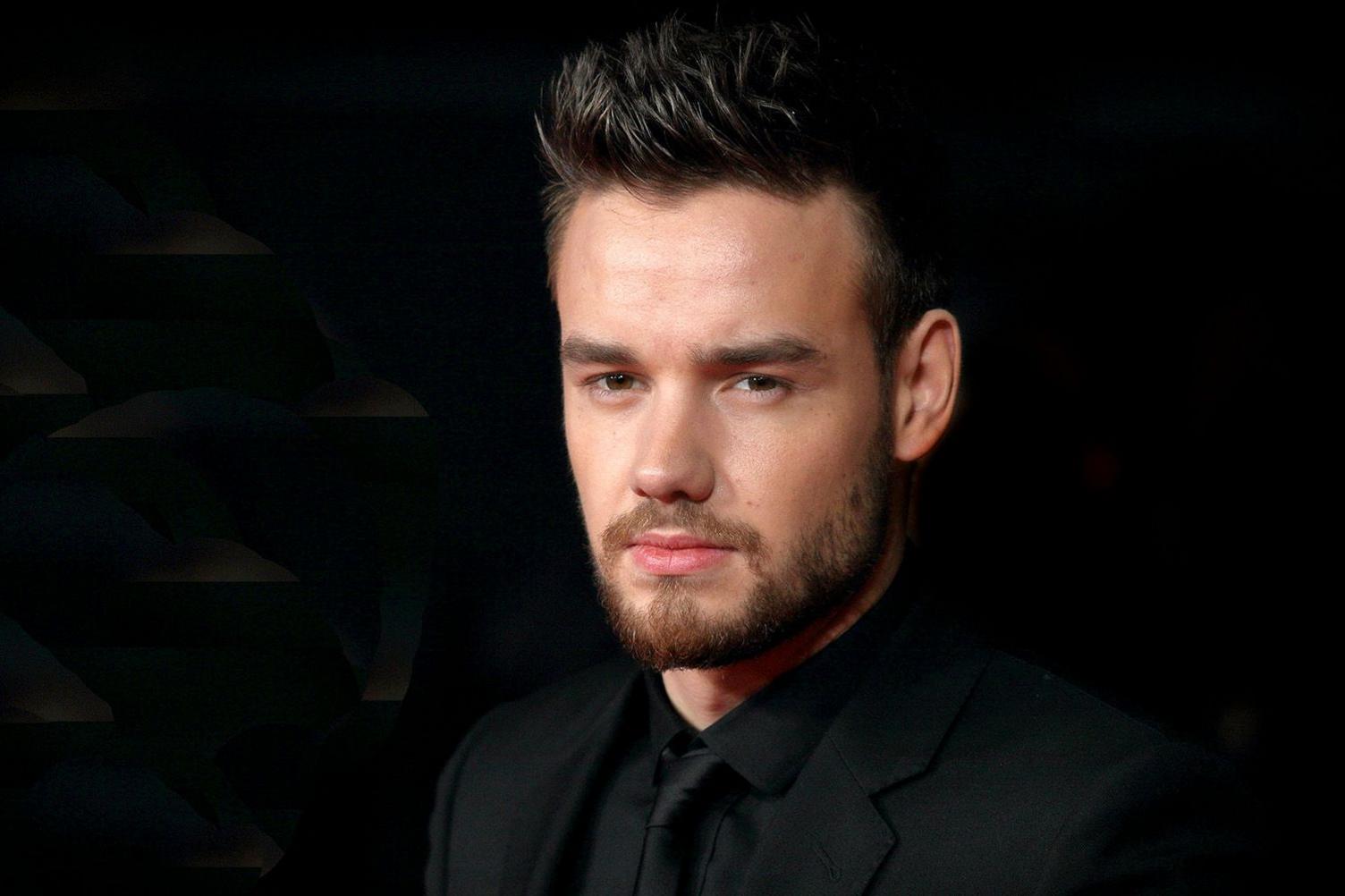 Publicity shot of Liam Payne wearing black against a black background. He has gelled hair and a neat beard and is looking moodily into the camera.