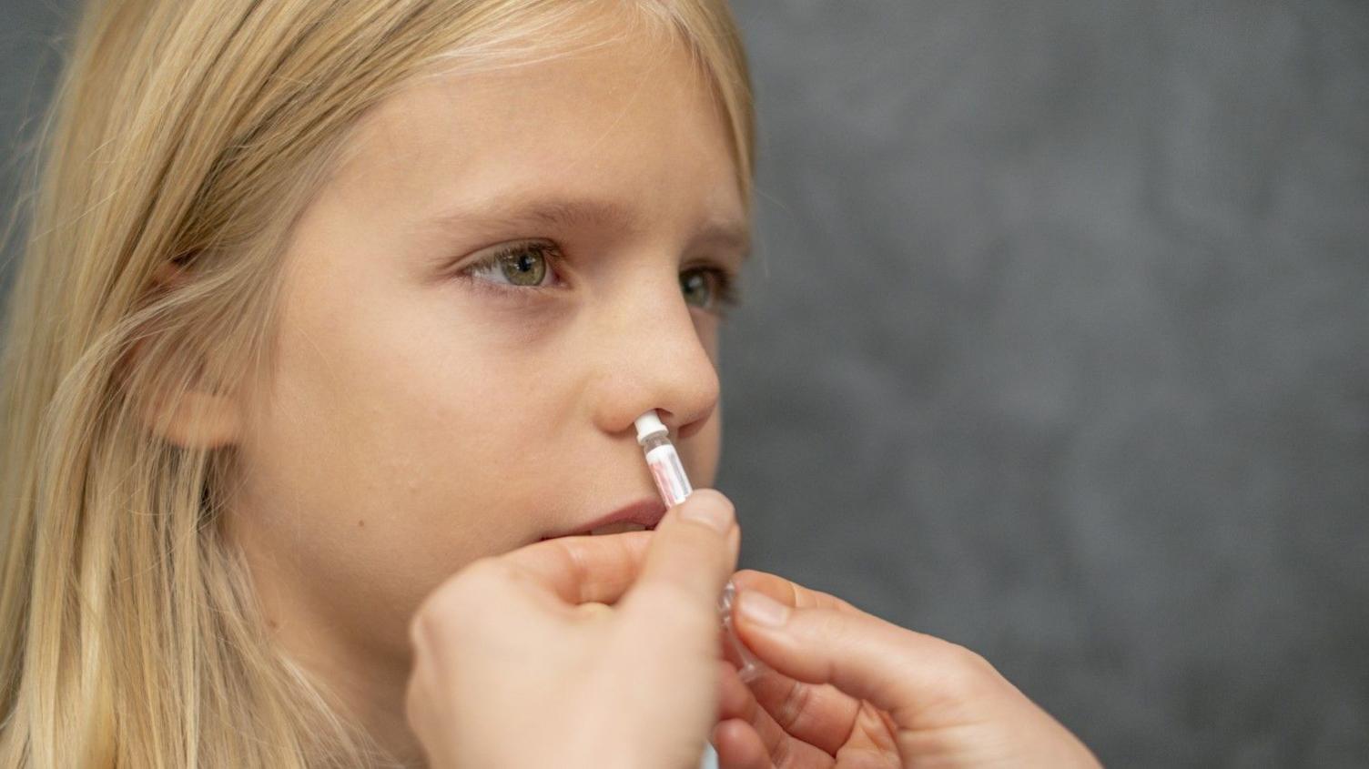 Child with long hair being given a nasal vaccine.