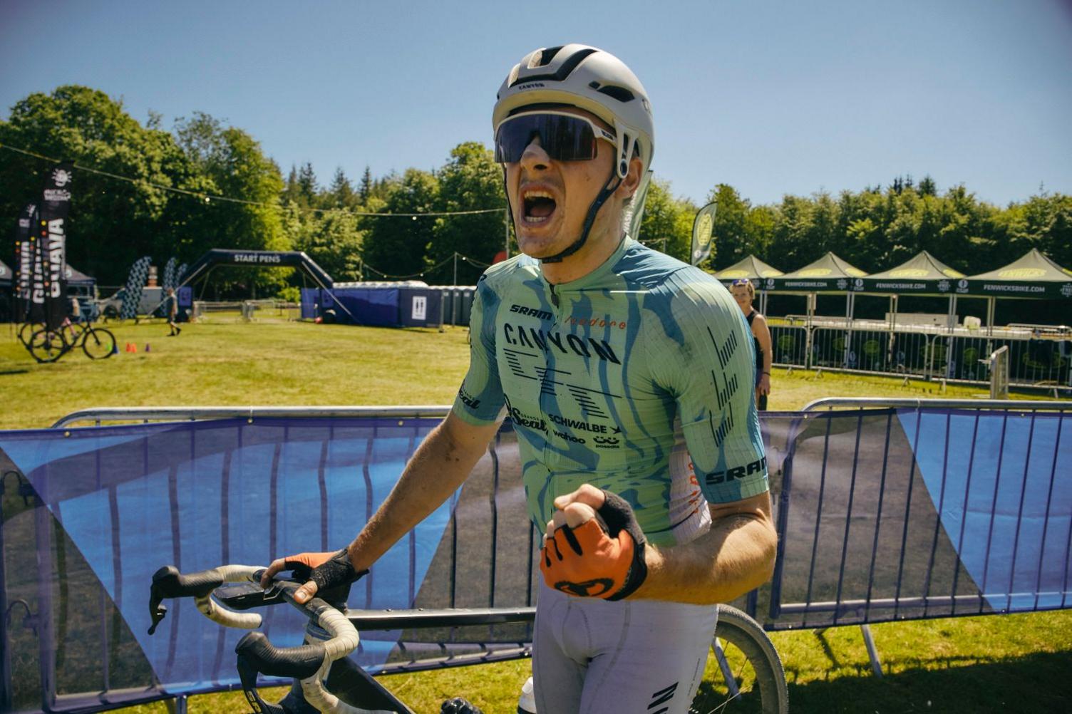A cyclist in a green top and dark glasses punches the air in celebration