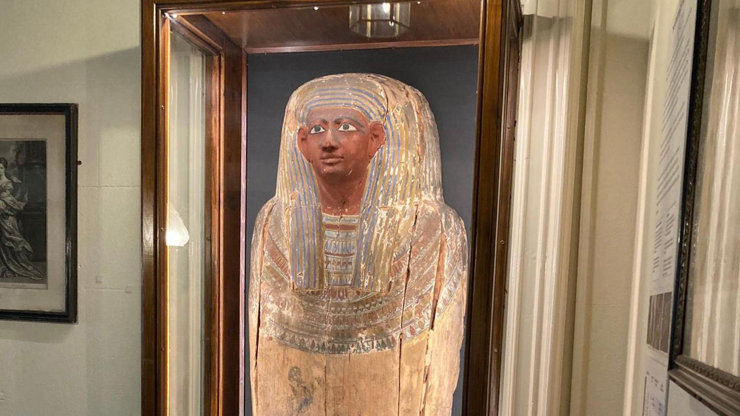 An ancient Egyptian coffin lid which depicts the effigy of a person. It is yellow, brown and blue in colour.