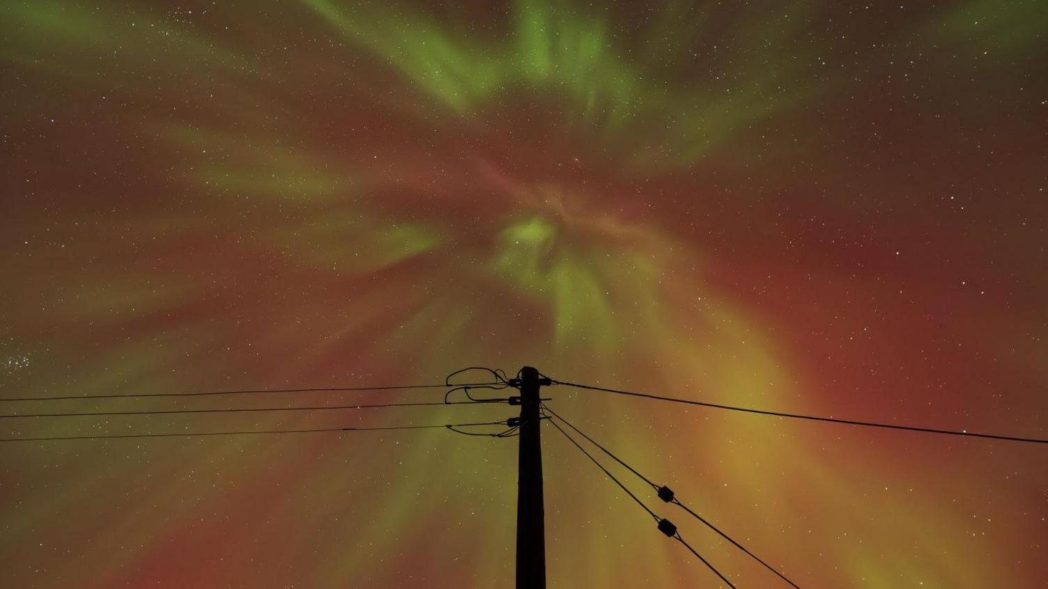 An aurora corona appears overhead. There is an electricity pole with cables going from it.