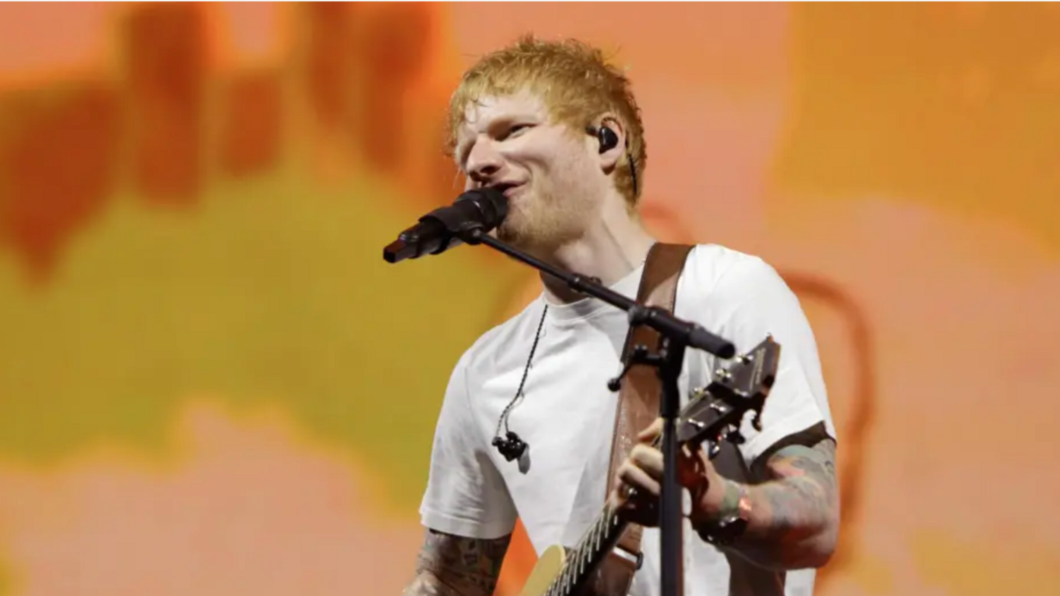 Ed Sheeran on stage in front of yellow and orange background