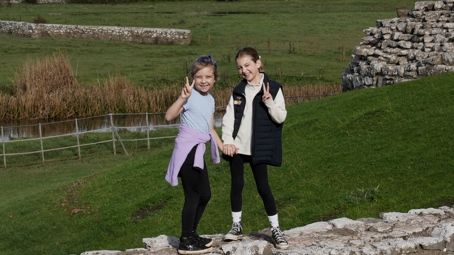 Betsy and Tilly, in the grounds of Ogmore castle,  holding hands and smiling at the camera