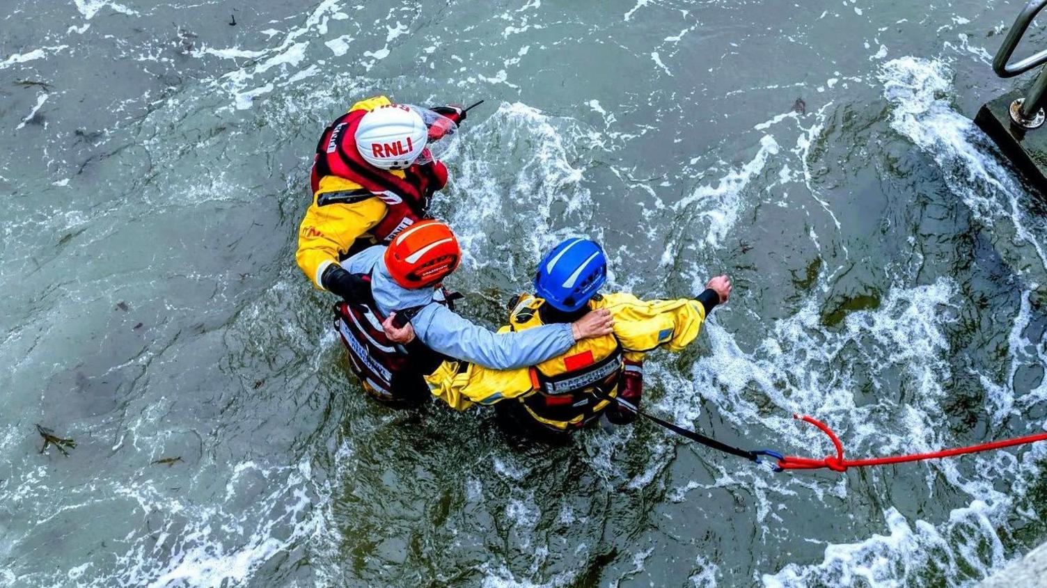 HM Coastguard and RNLI crew escort a casualty to safety using a rope, as they near the sea wall.