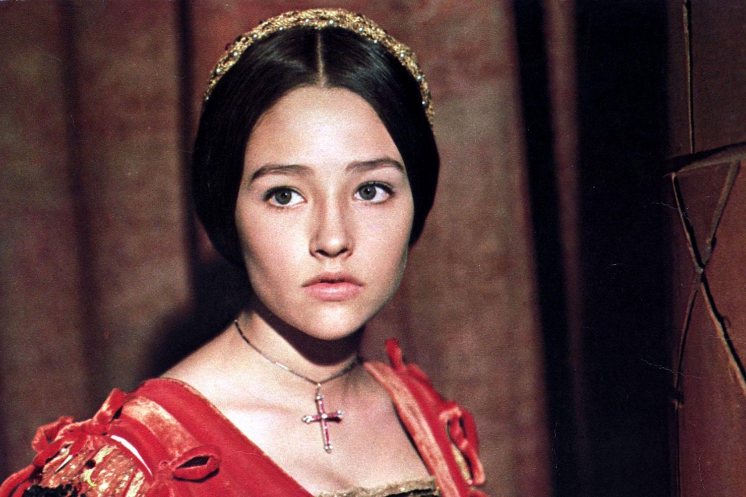 Olivia Hussey dressed as Juliet, wearing a red dress and a gold cross necklace. 