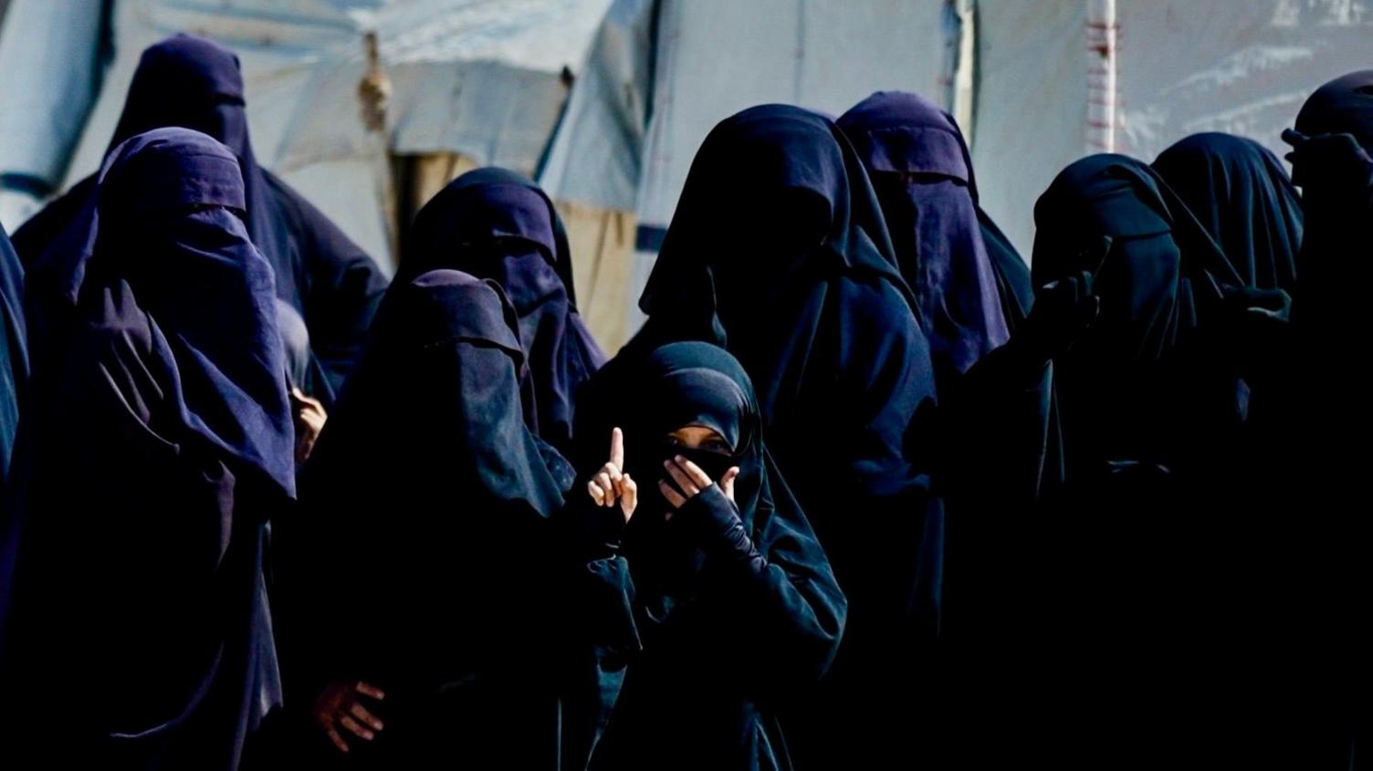 Several veiled women and children, clad head to toe in black, at the camp.