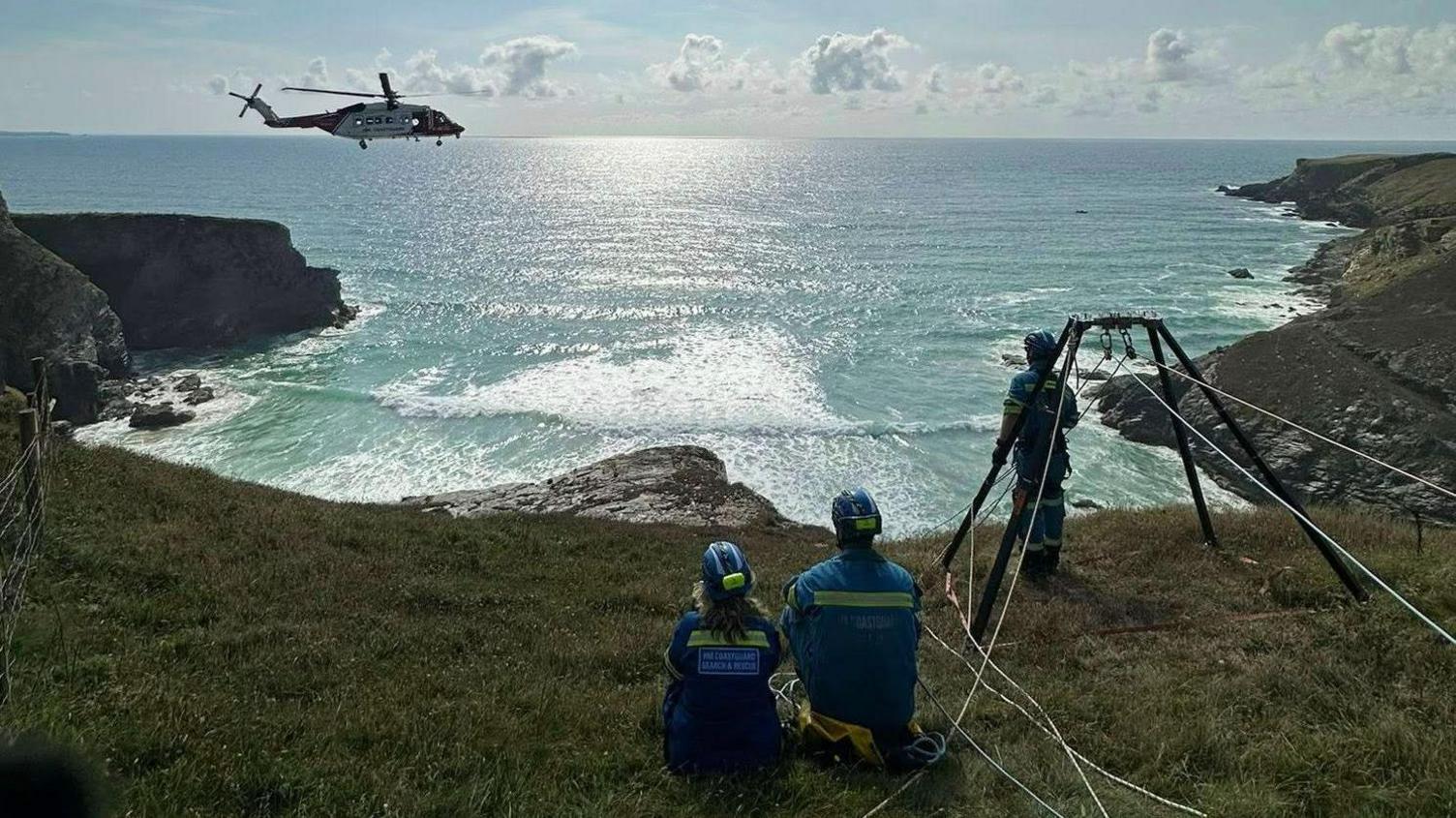 Members of a rescue team on top of a cliff. A helicopter is flying above them.