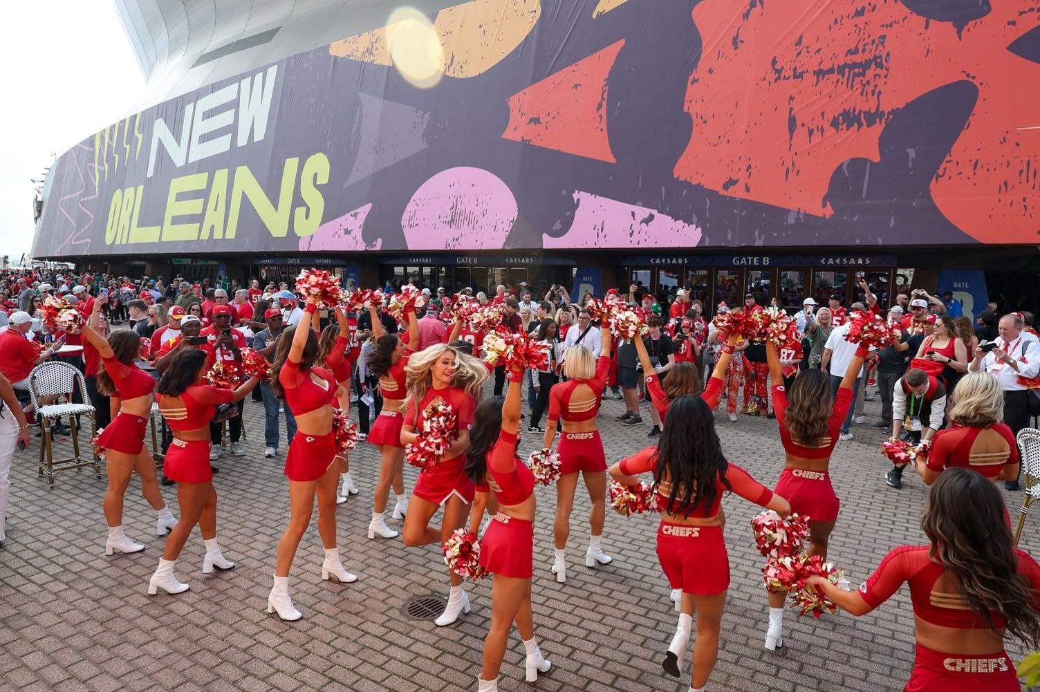 Cheerleaders in front of a crowd in front of a stadium with a large sign that says "New Orleans"