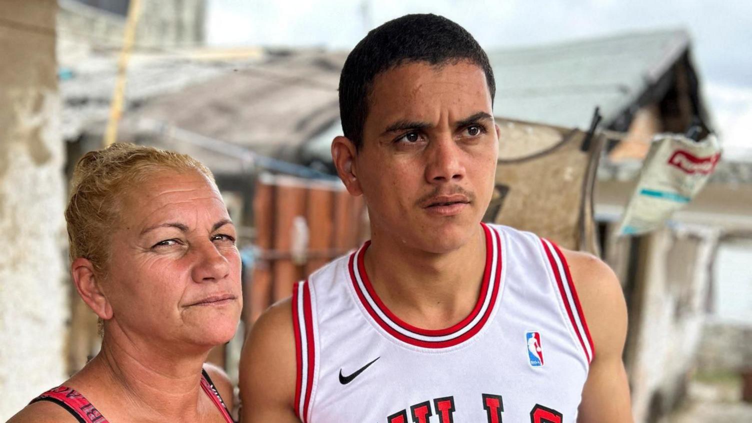 Dariel Cruz, 23, flanked by his mother Yaquelinz, speaks to Reuters in their home in Havana, Cuba, 15 January 2025