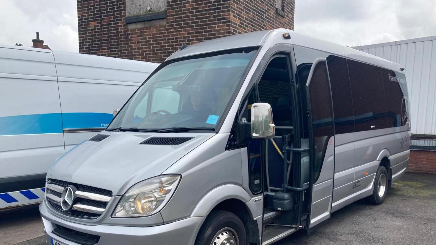 Photo of a silver Mercedes minibus. The vehicle is parked in a car park with its passenger door open.