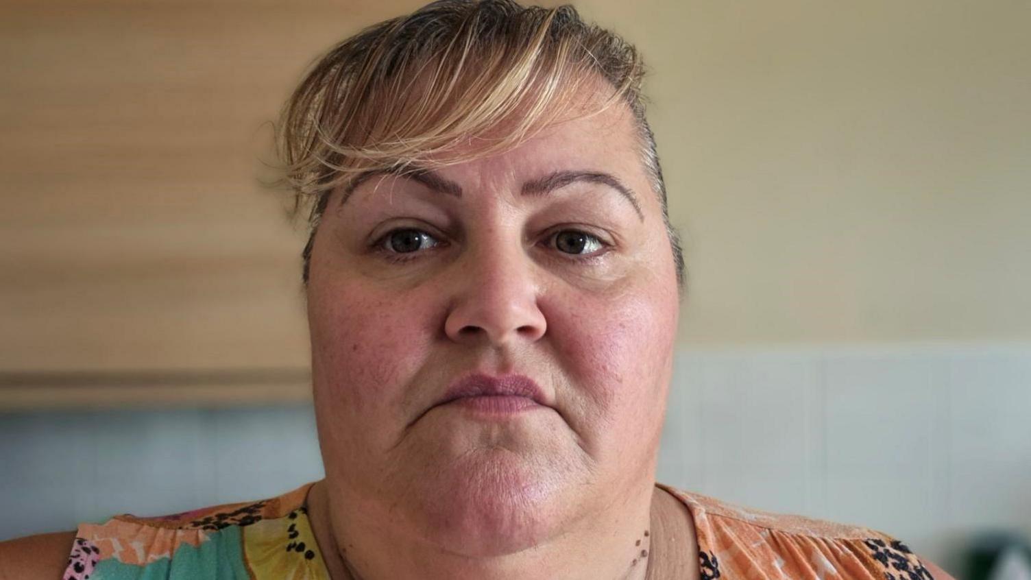 A woman with a fringe looks directly into camera with a serious expression