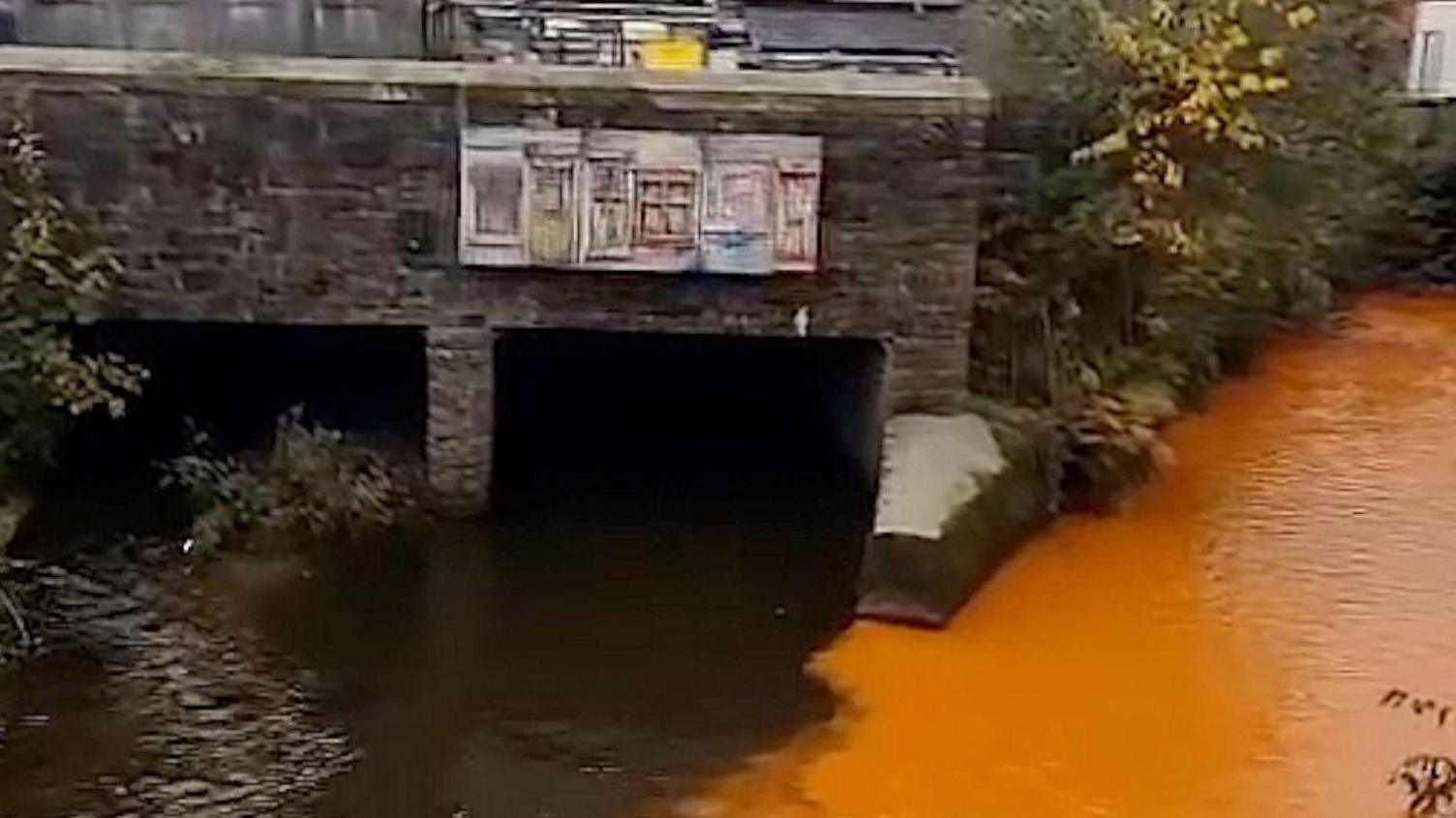 Water in the River Calder at Todmorden which is heavily discoloured making it appear to be orange