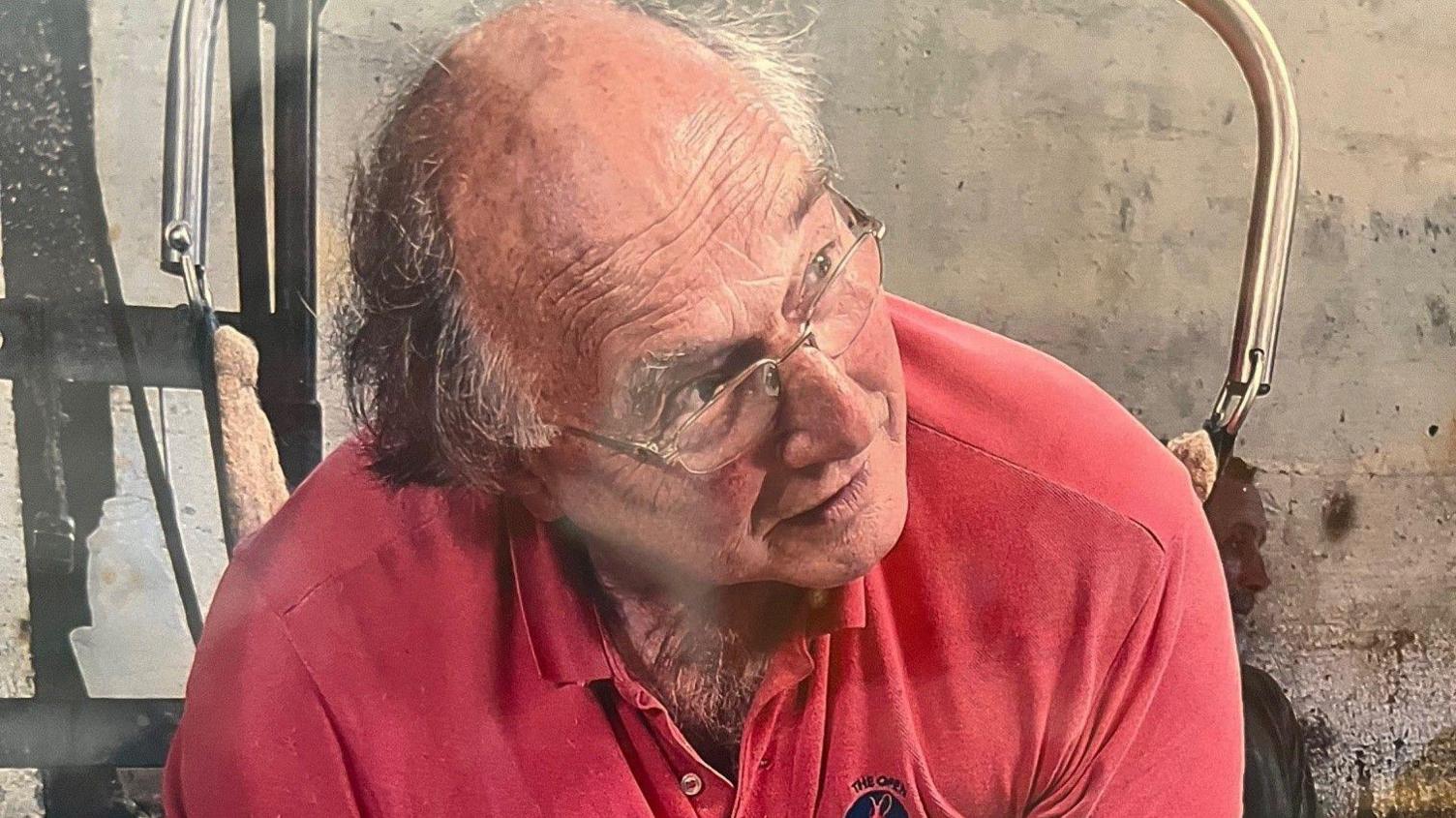 Eddie Gully, and balding man with glasses, is wearing a red polo shirt and leaning into a sheep shearing back support device.