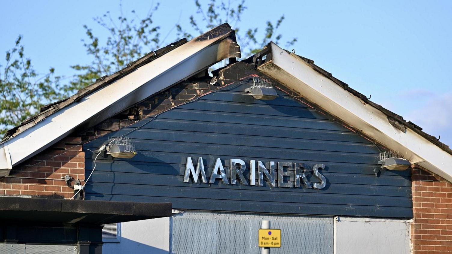 The damaged roof in daylight after the fire has been extinguished. The tiles have fallen in and the trims and brickwork are black and charred.