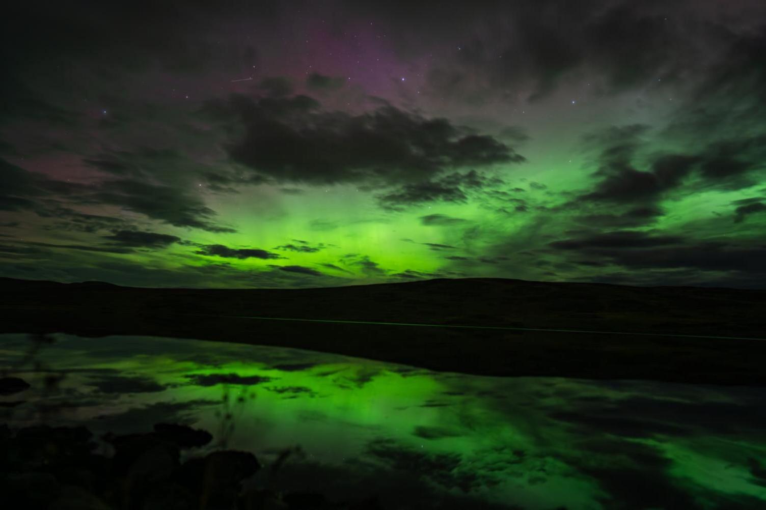 A green sky coloured by an aurora reflects into calm water at Bonar Bridge.