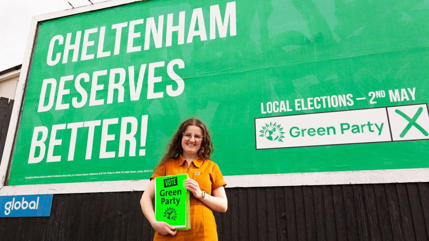 Ashleigh Davies standing in front of a green party billboard