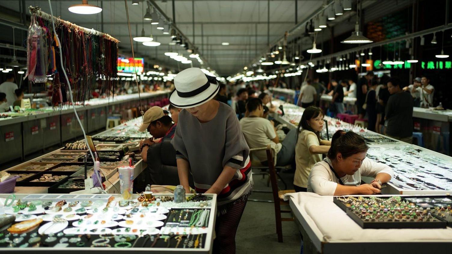 At Ruili market, women sit and stand next to stalls selling jewellery