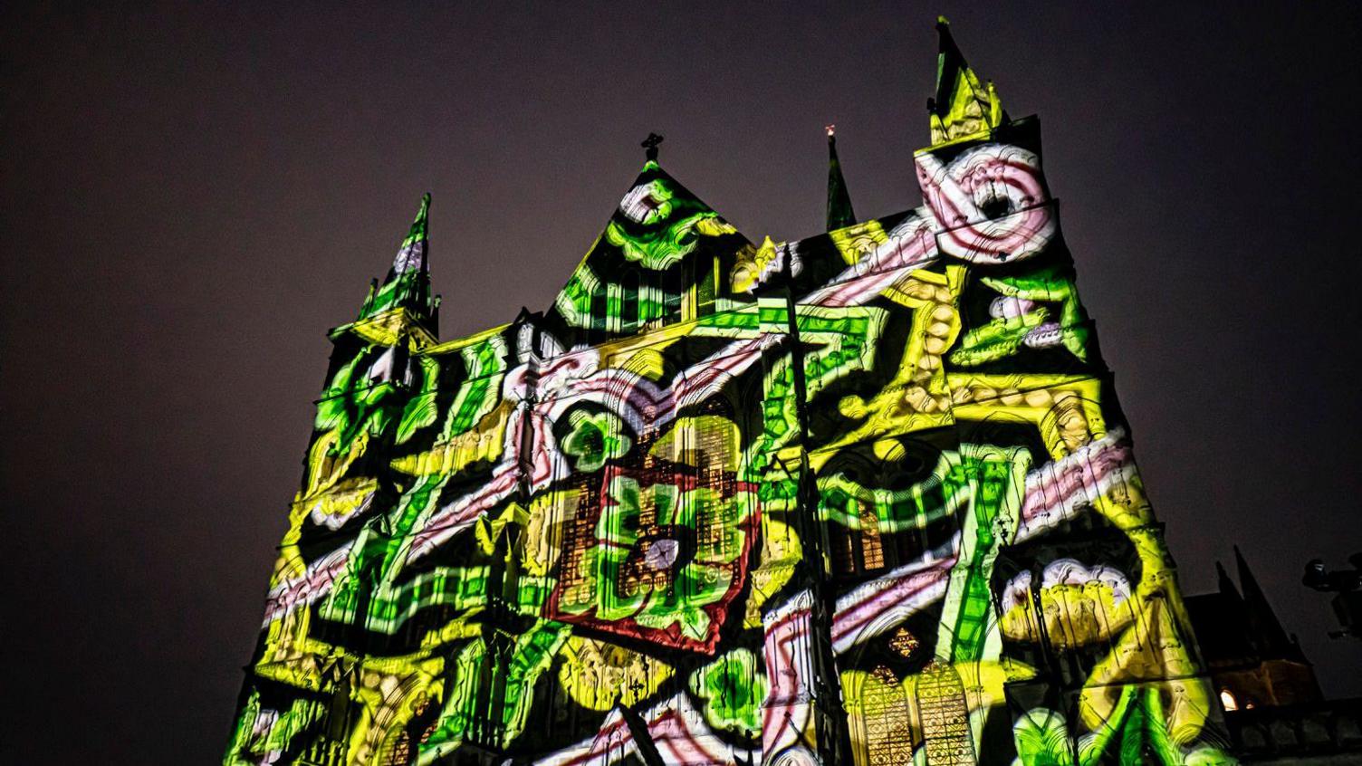 The front of Beverley Minster lit up with green, yellow, white and red patterns.