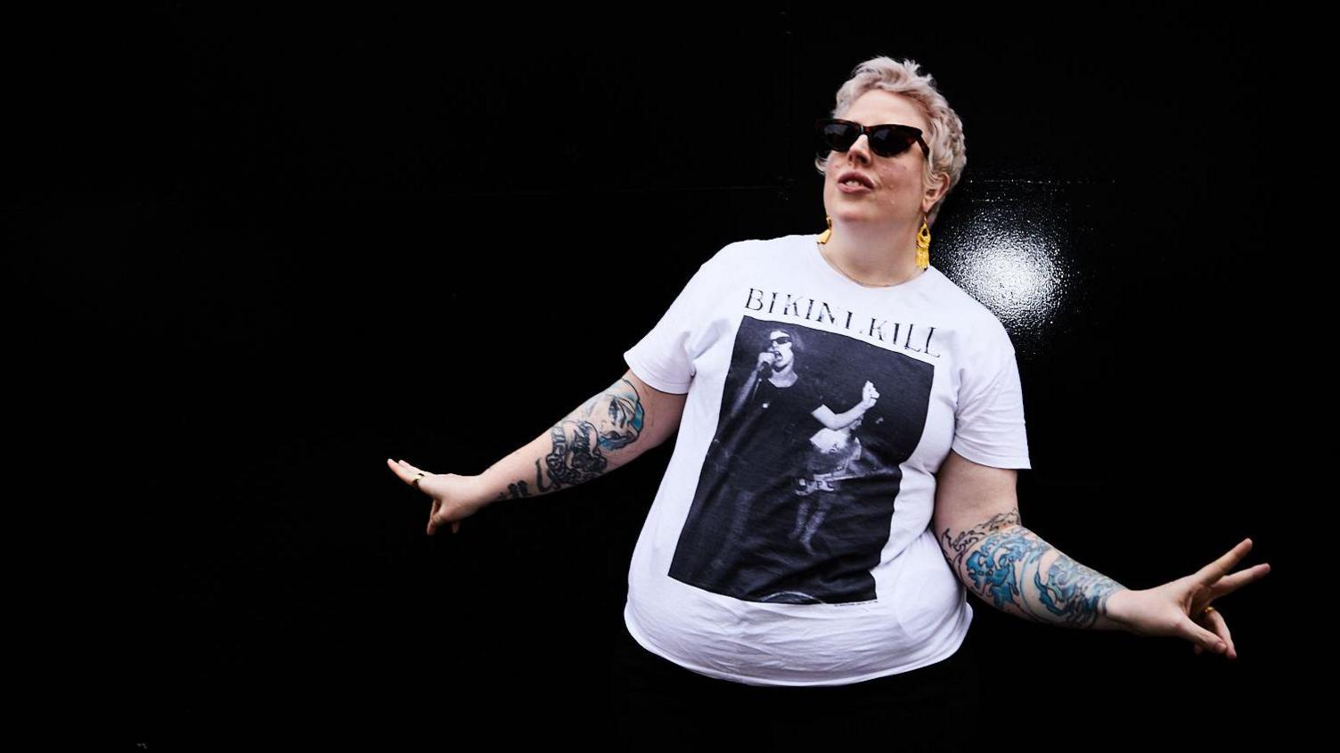 Marea Stamper, aka The Blessed Madonna wearing a pair of dark sunglasses and a white tshirt, with the tattoos on her arms on display