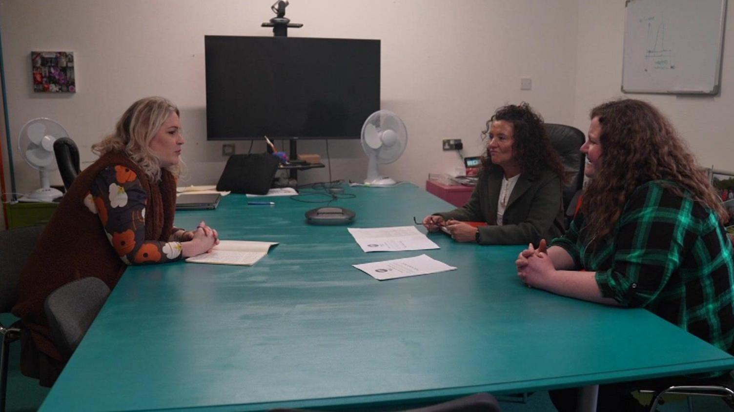 Three women sit around a big table talking