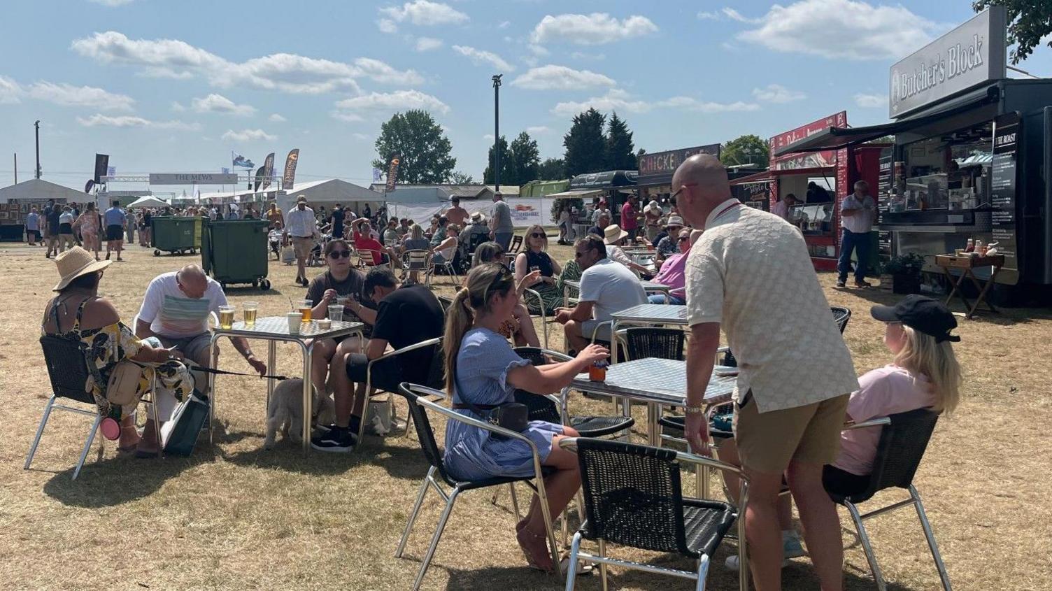People sat at tables having refreshments. There are a number of food and drink stalls in the background.