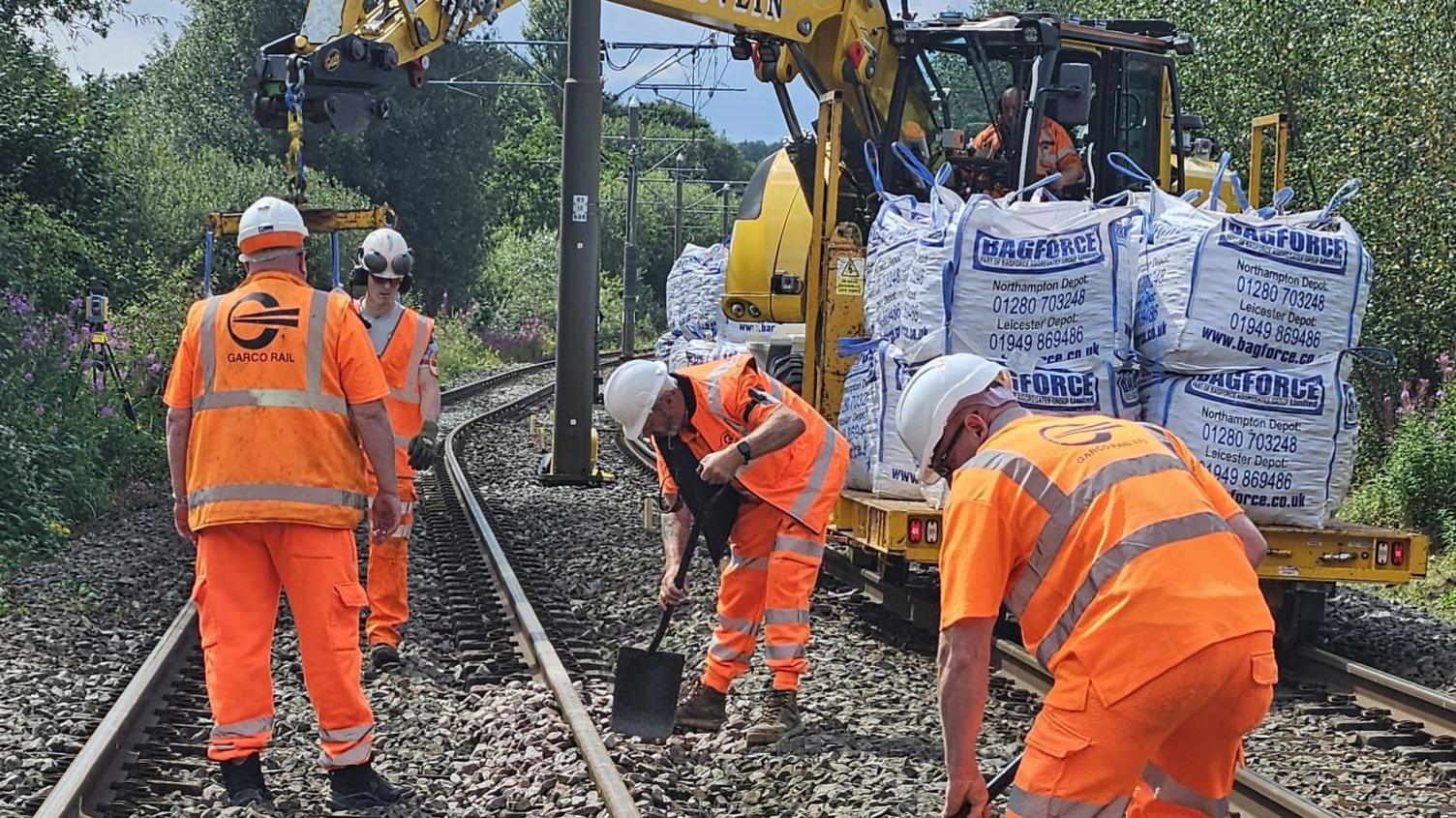 Men in orange work gear use shovels to put down hardcore on a section of the tramway between Oldham and Rochdale. 