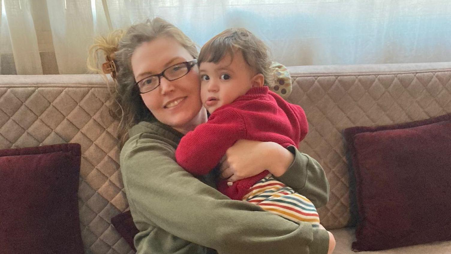 Catherine Flanagan with her son David. She is wearing glasses and a green jumper. David, wearing a red cardigan, hugs his mother and looks at the camera. 