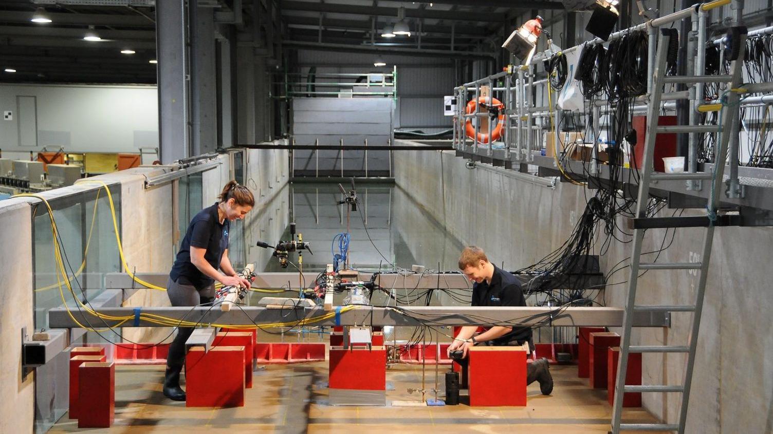 A man and a woman wearing blue polo shirts assembling some electrical equipment on a concrete bank next to a trough of water.