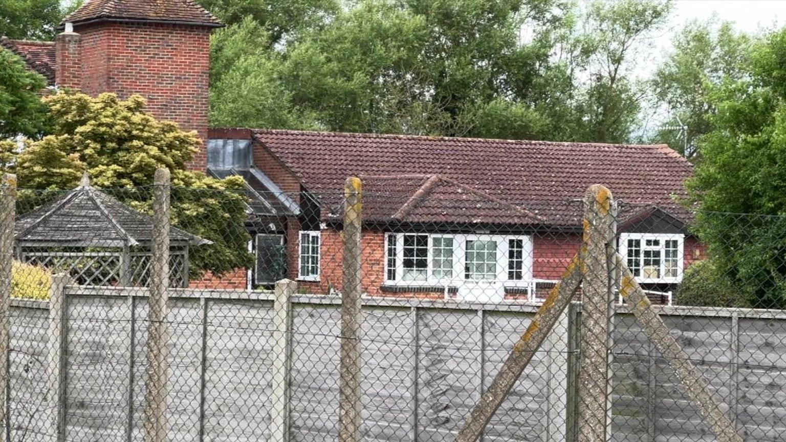 Parrot farmhouse, a red brick building seen through a fence in Shinfield