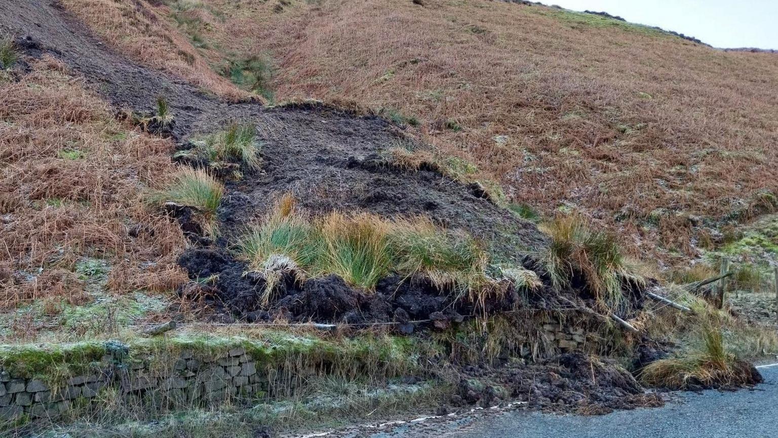 The landslip on the A59 at Kex Gill - a road with a dry stone wall and earth shown falling over the top onto the road 