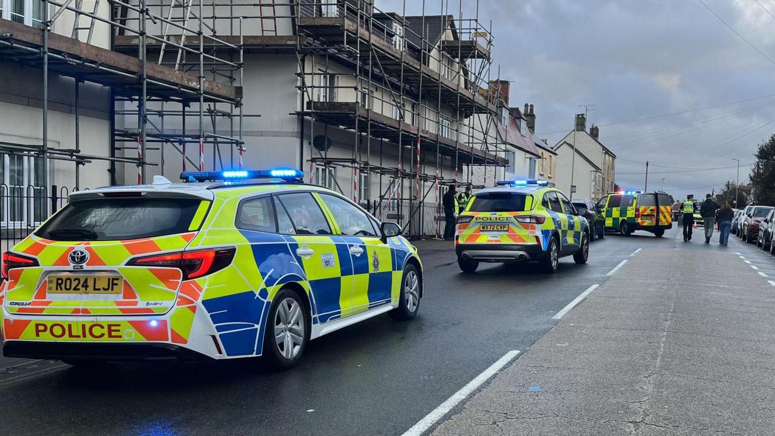 London Road in Chippenham with houses on either side and cars parked. There are three police cars with sirens that are parked on the road.