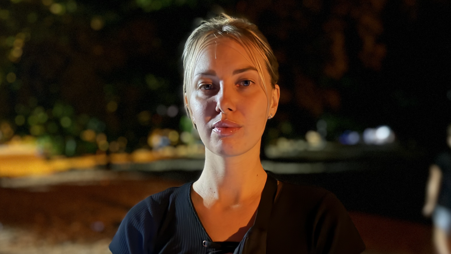 Head and shoulders shot of a woman with blonde air, tied back, wearing a black t-shirt. 