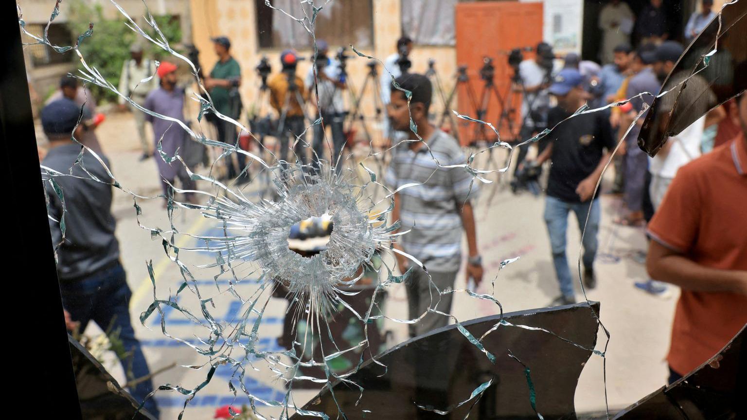 Men in plain clothes and some in police uniform are seen through a broken glass window with a hole created by some sort of impact.