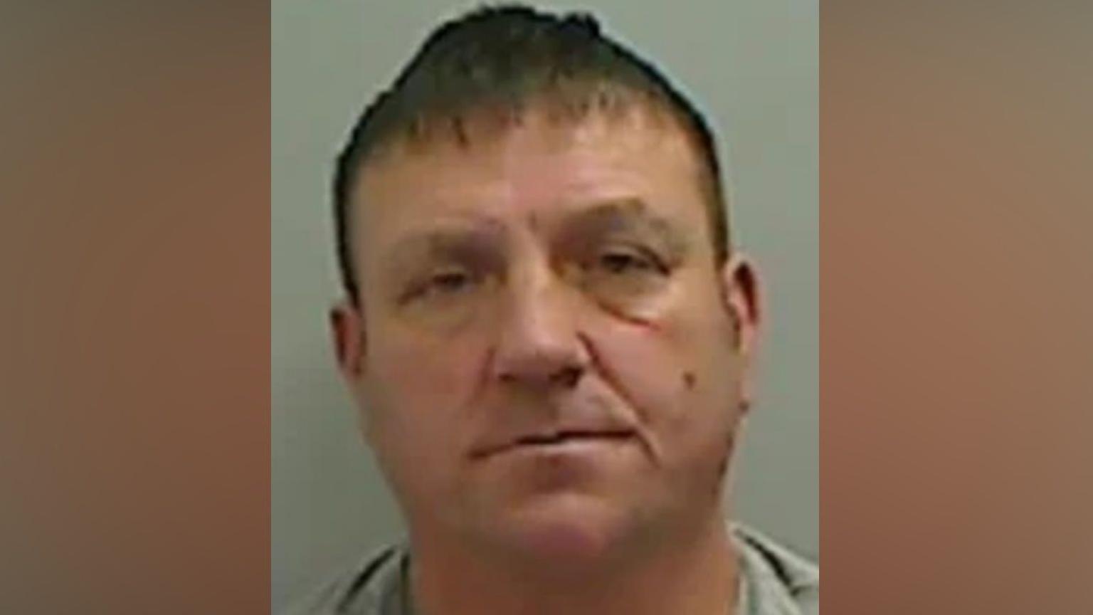 Mugshot of Pearce. He is white, clean shaven, of a stocky build and has short brown hair.