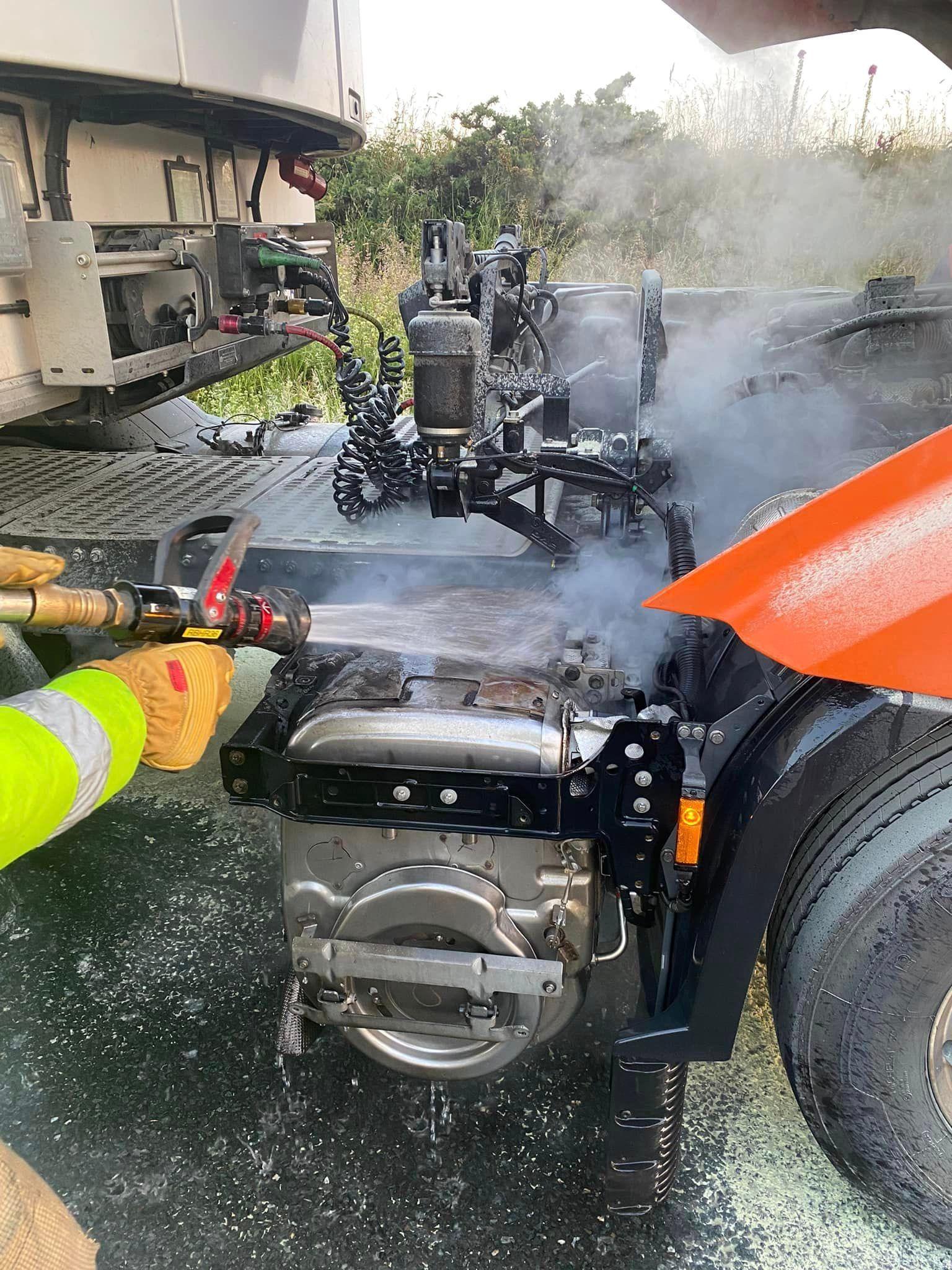 A fire fighter sprays a liquid on a piece of machinery between the cab and truck of an HGV.