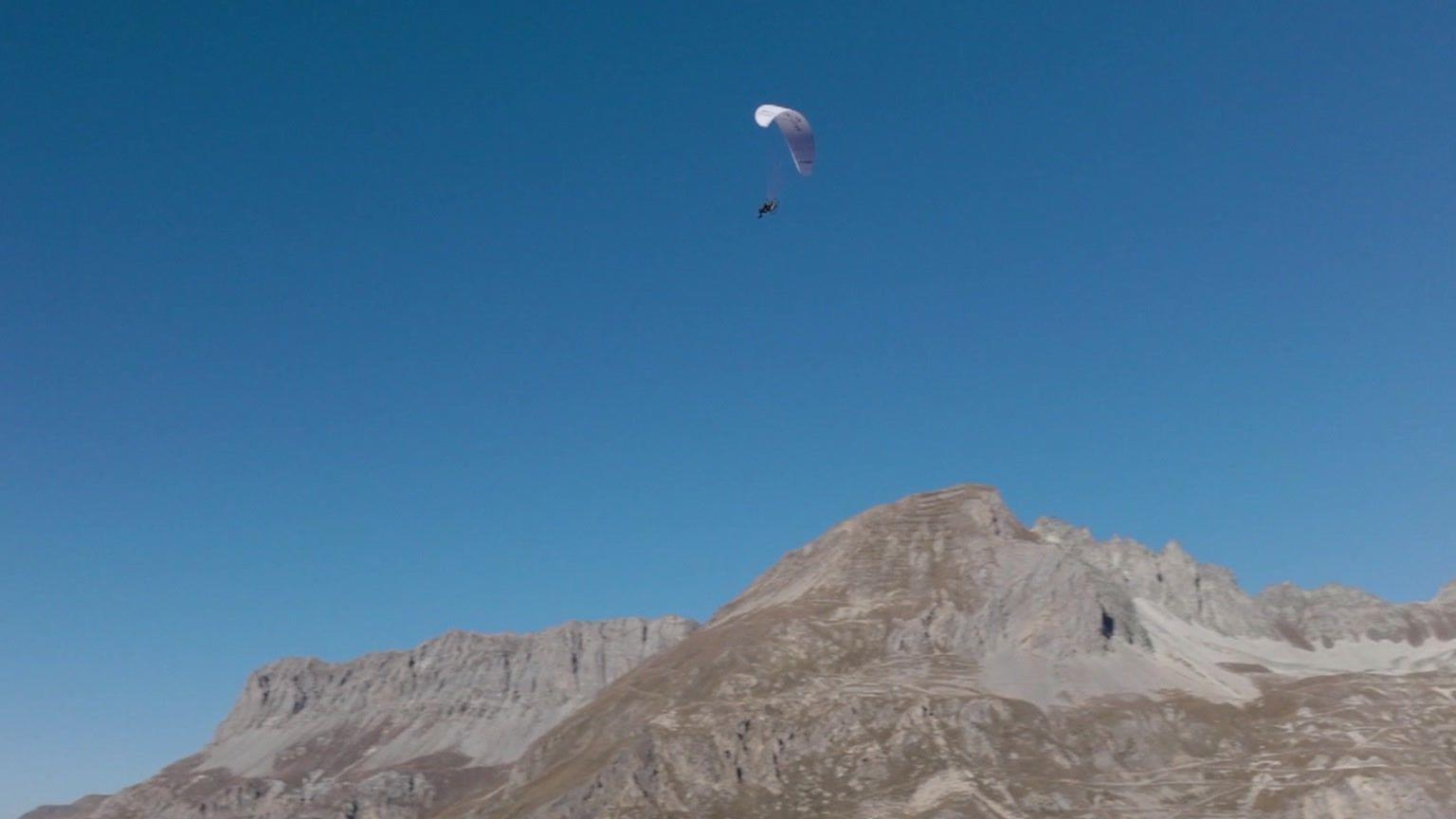 A blue sky is seen with the twins in the air with the paraglider above the French Alps