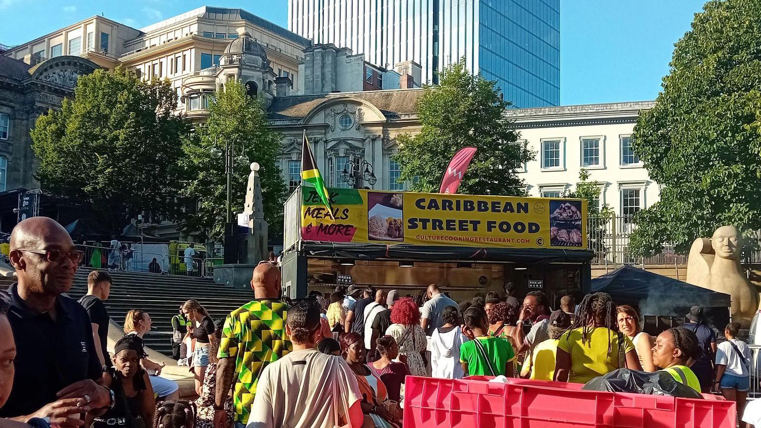 A crowd of people at the 0121 Jamaica festival. They are queuing in front of a stall with a sign saying "Caribbean Street Food"