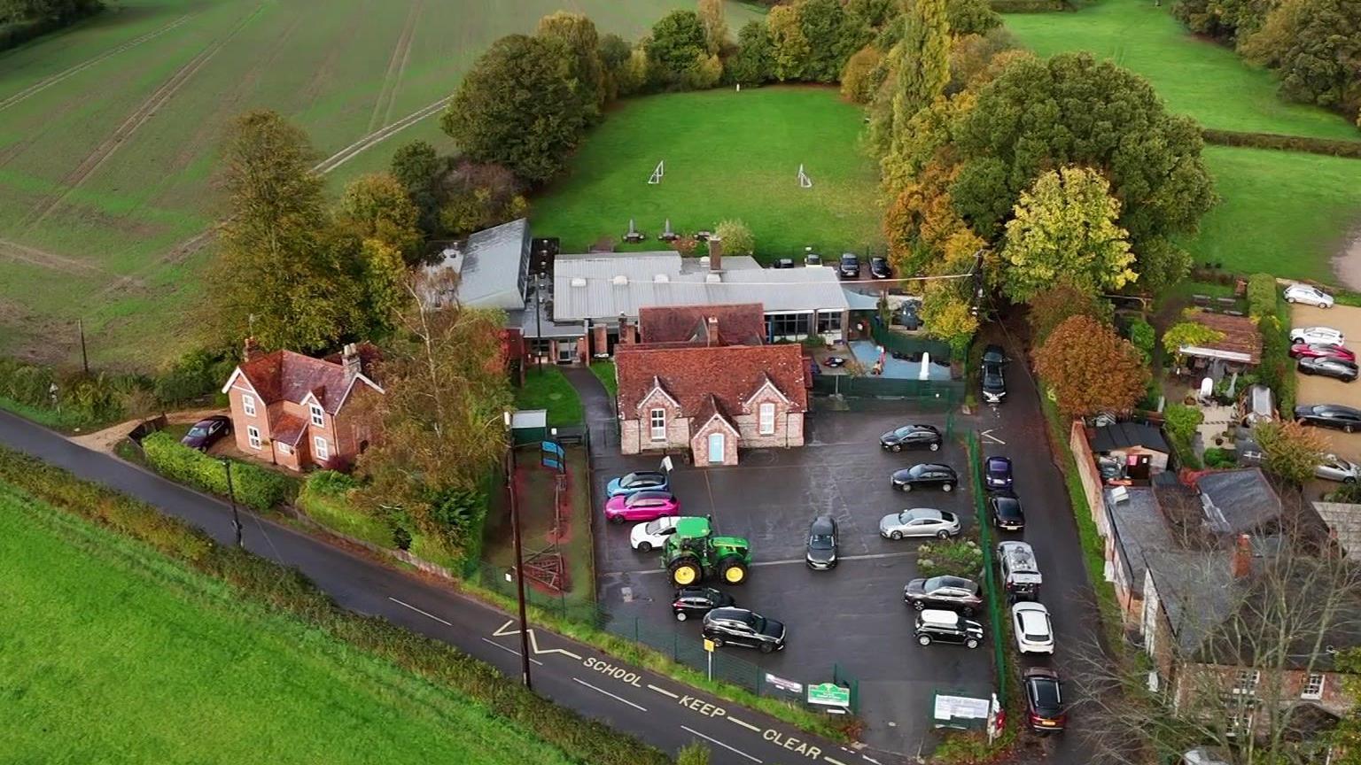 The school from above, a small red-bricked building with a newer building and field behind it.