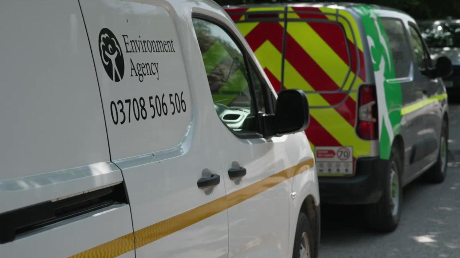 Two vans including a white one with a sign and another with hi-vis markings.