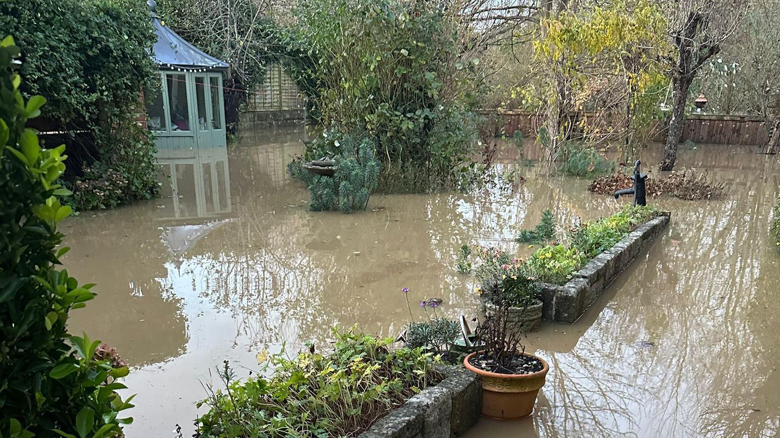 flooded back garden with planters and trees inundated with water - summer house in background